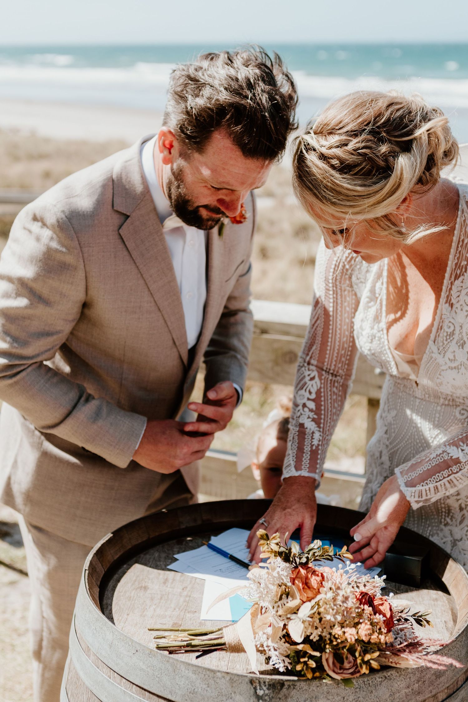 Couple sharing a laugh while looking at their beach wedding bouquet. Papamoa Surf Lifesaving Club Wedding
