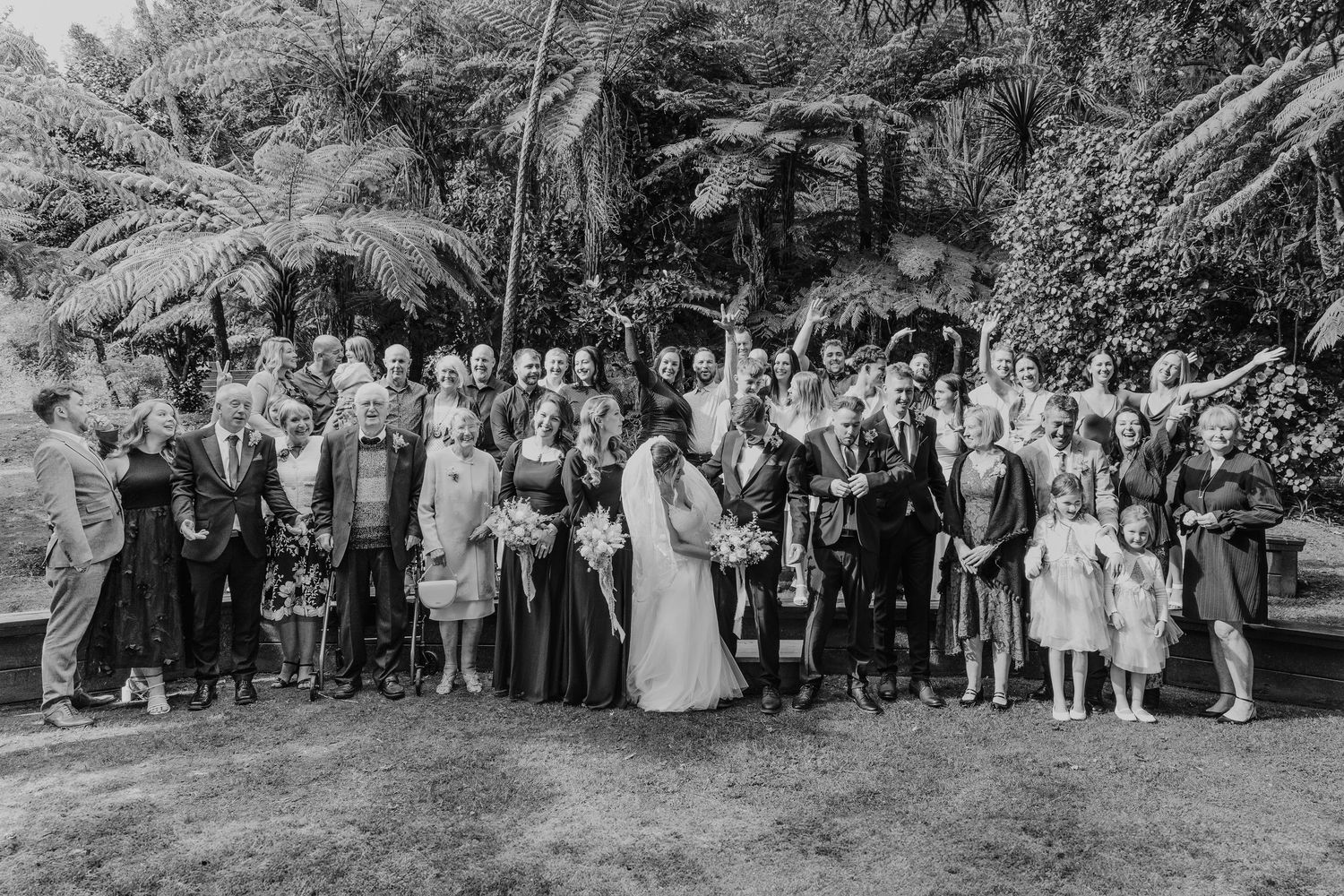 Large wedding party group photo outdoors with palm trees in black and white.