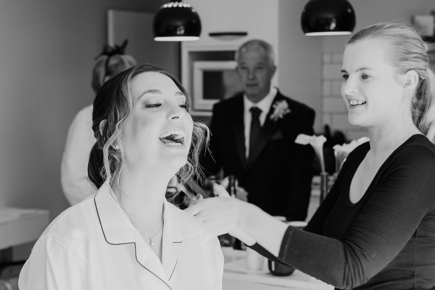 Black and white candid shot of wedding preparations with joyful expressions.