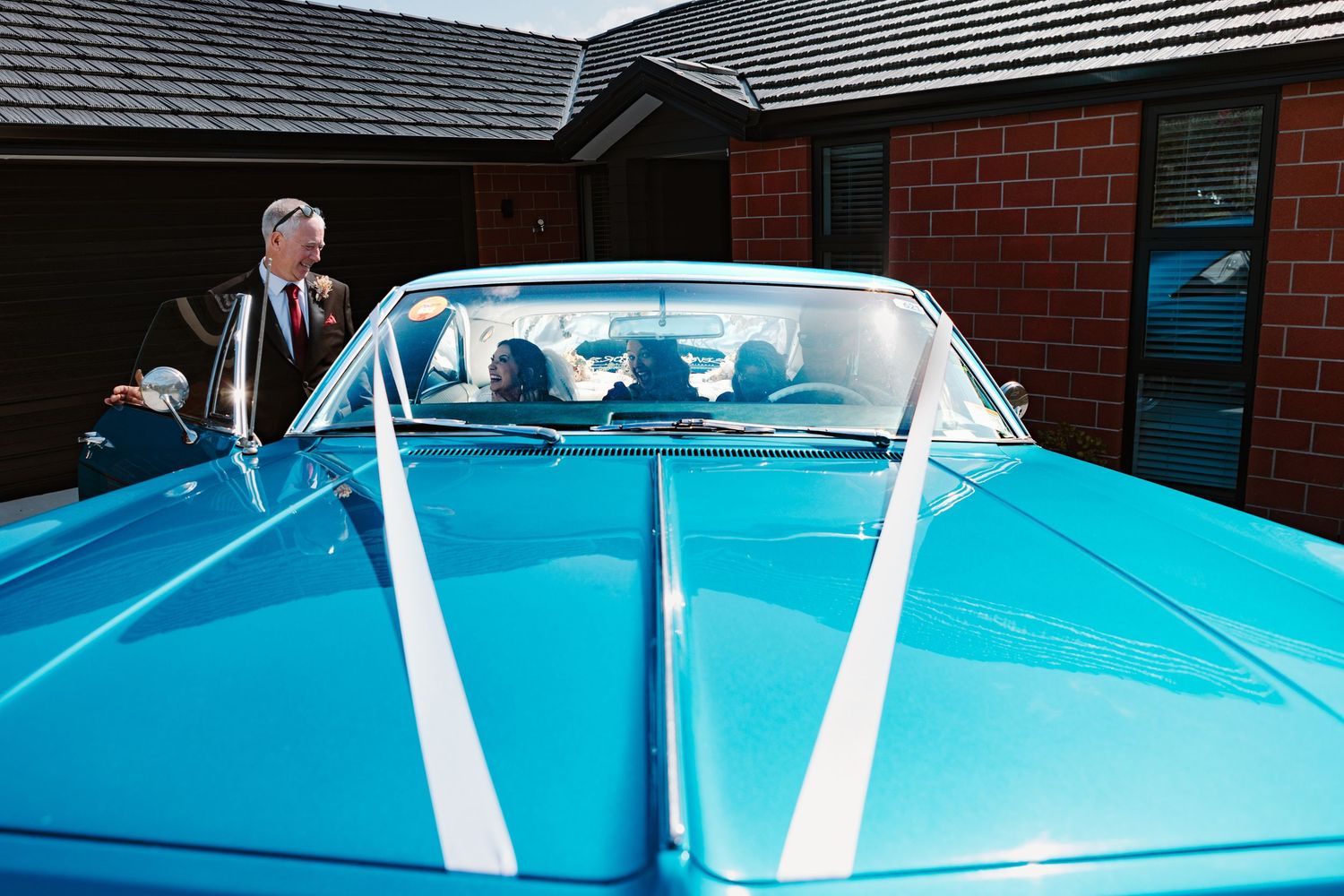 A close-up view of the hood and windshield of a classic turquoise blue car with white trim details.