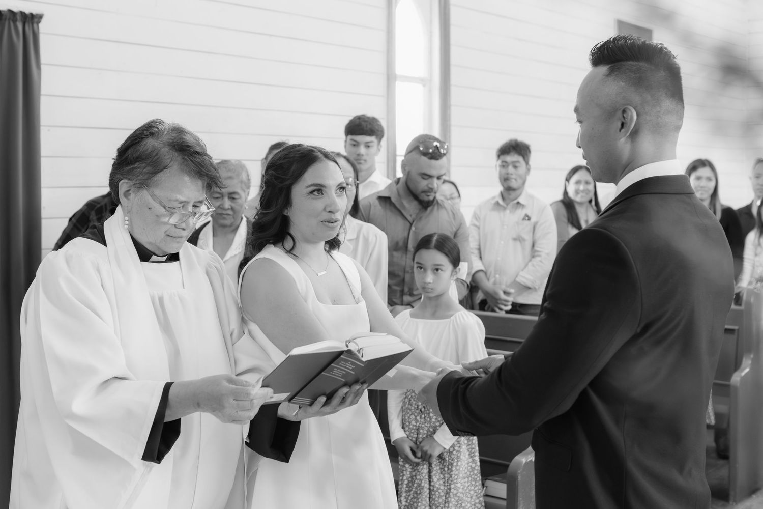 Black and white photo captures intimate wedding ceremony moment with guests in attendance.