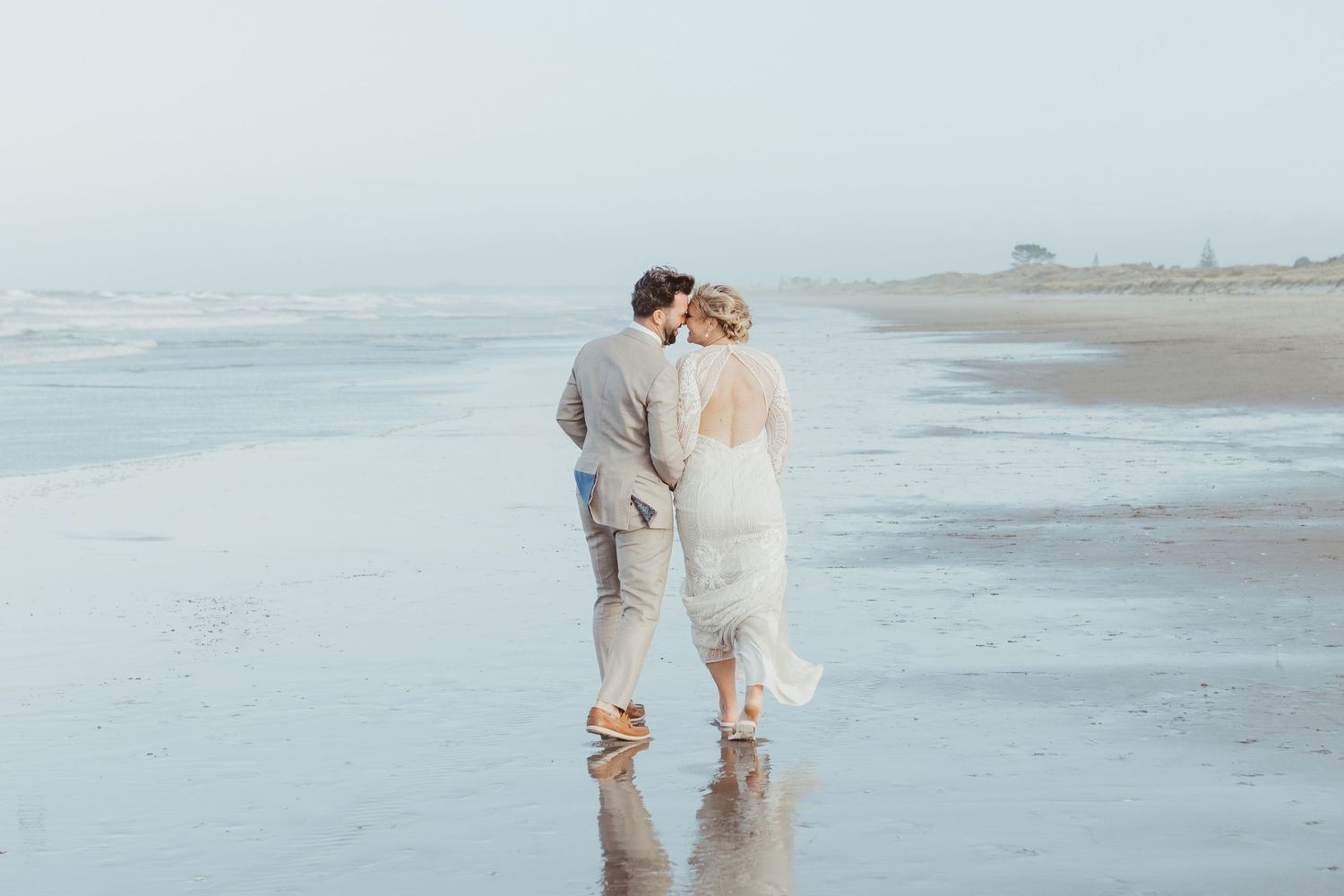 Newlyweds walking together on misty beach shoreline.