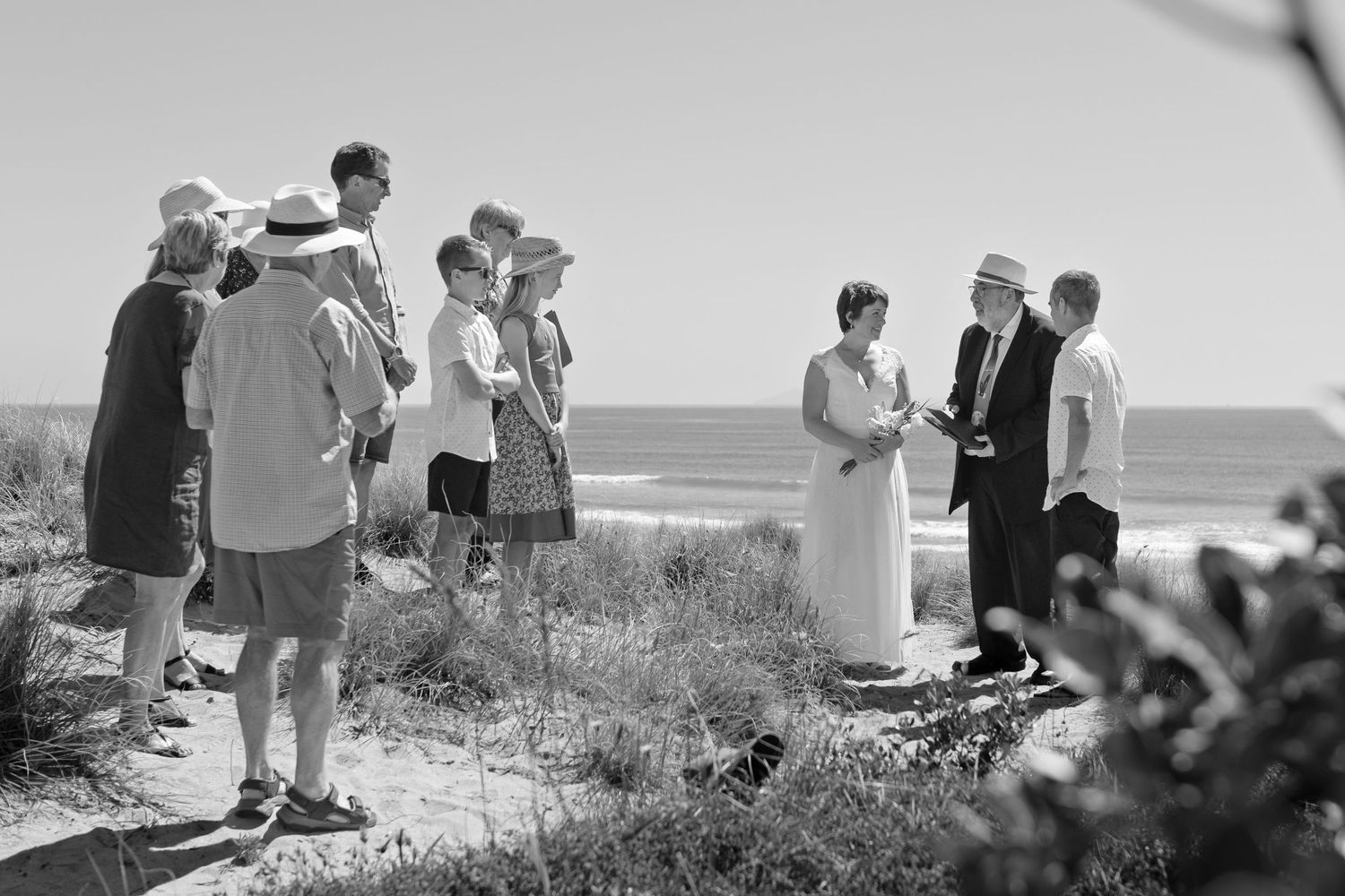 Black and white photograph of wedding guests mingling on a beachfront path.