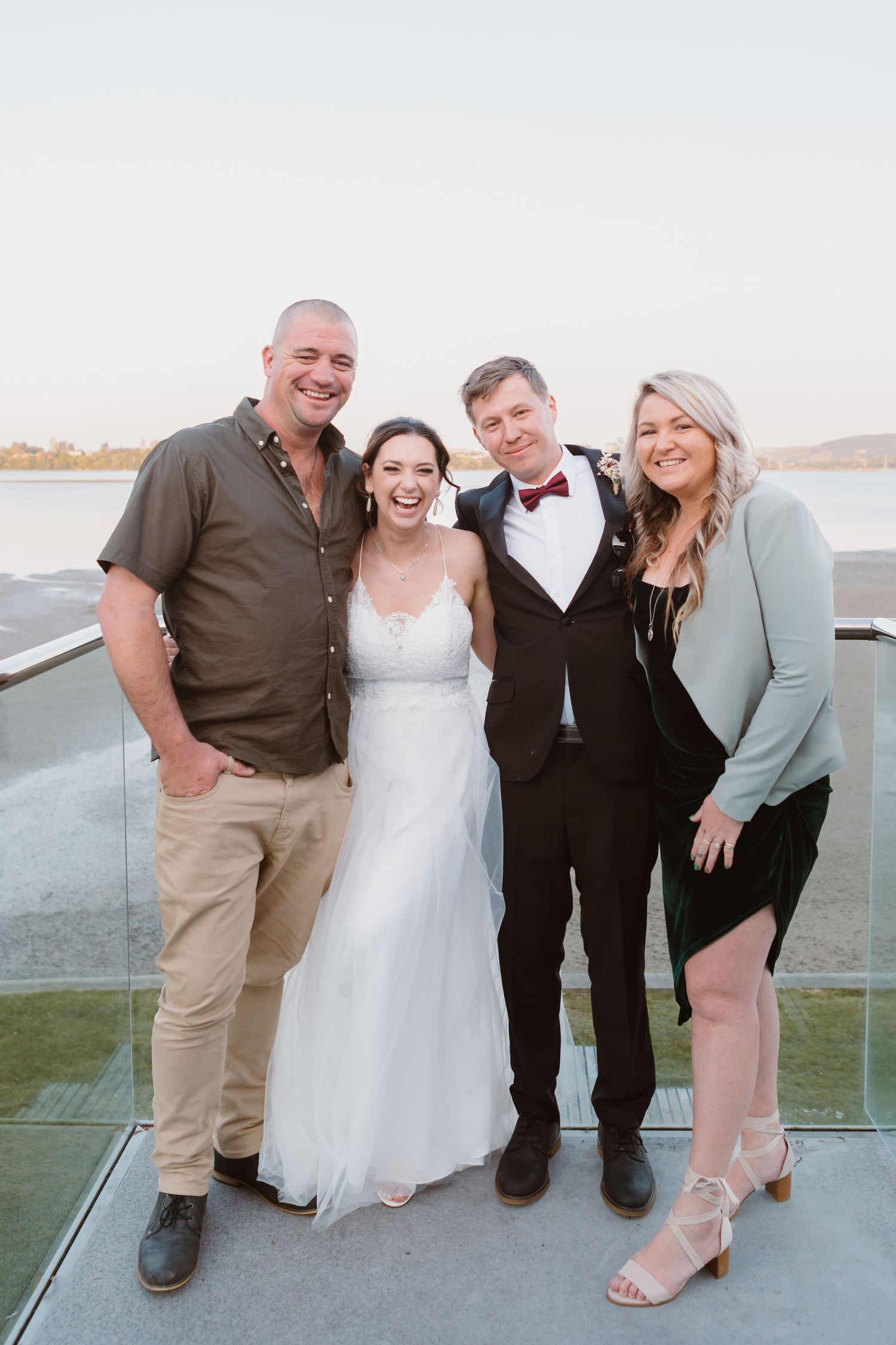 Wedding party gathers for informal group photos on a waterfront terrace.