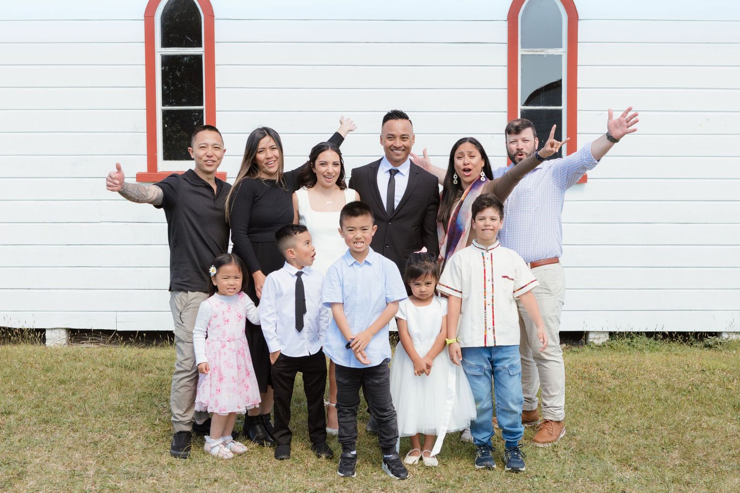 A large family group poses joyfully in front of a white church building.