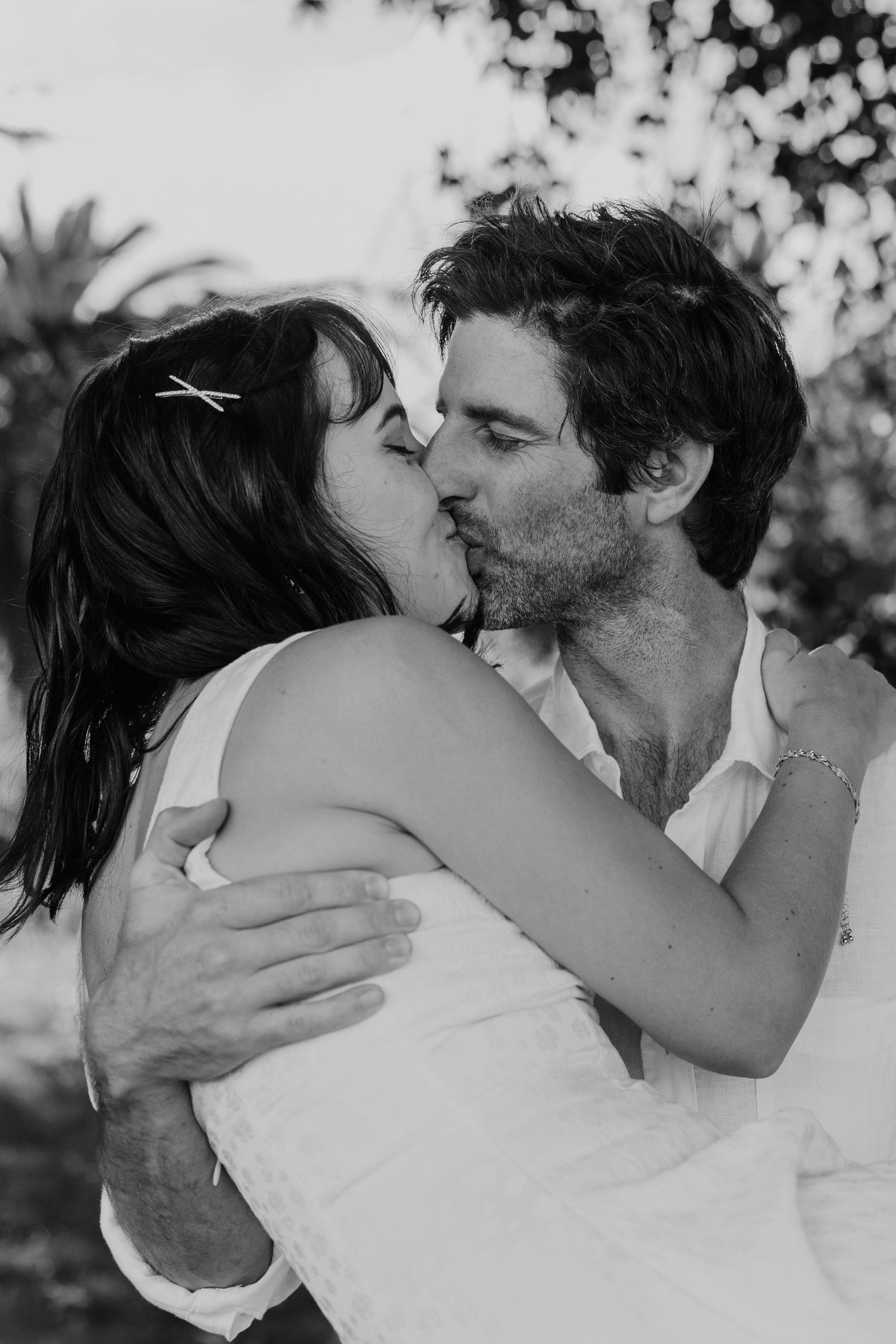 Black and white photo of a couple sharing a romantic kiss outdoors, embracing each other tenderly.