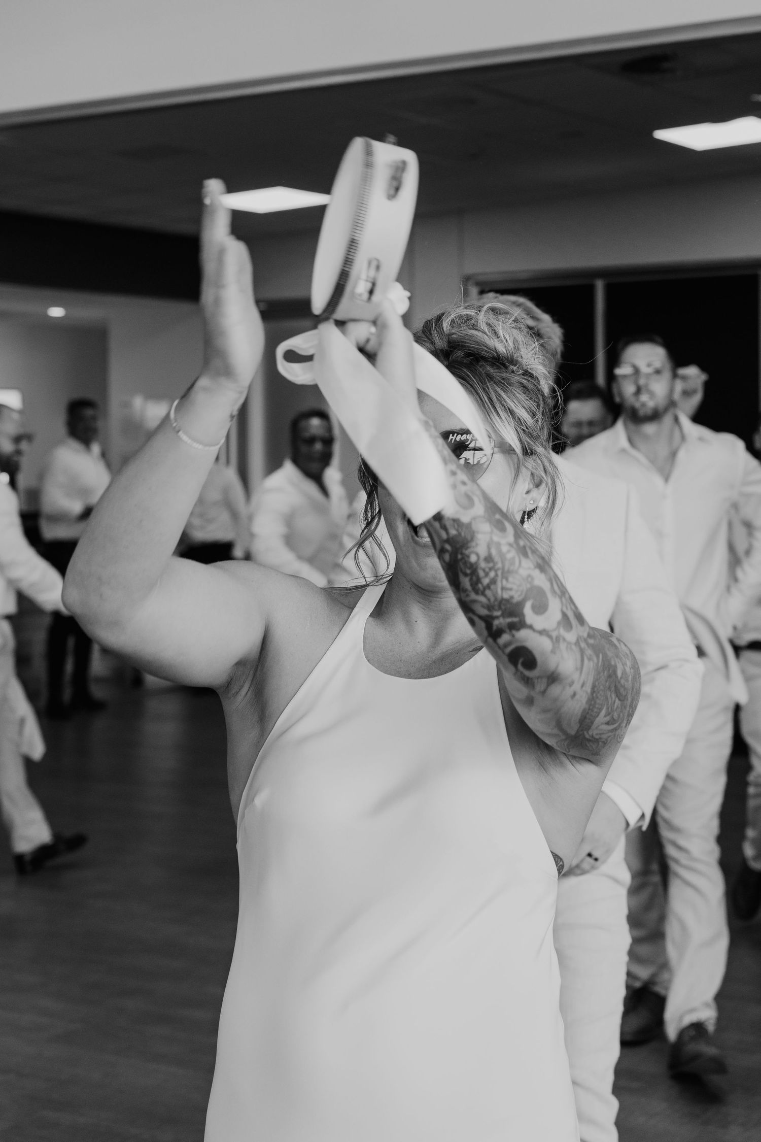 Black and white photo of a tattooed bride drinking from a shoe at her wedding reception.
