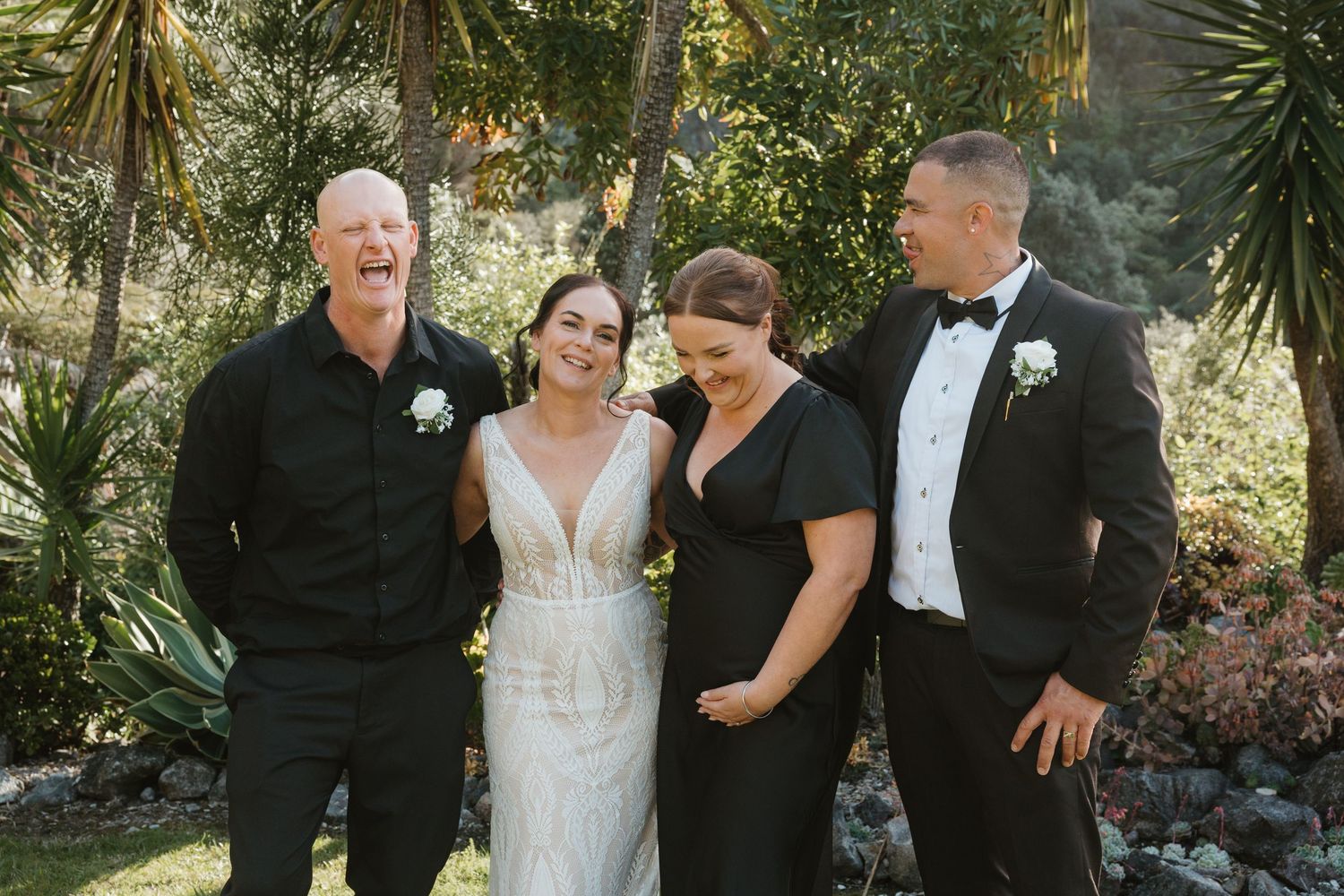A group of people in formal attire gather together for outdoor wedding photos in a garden setting.