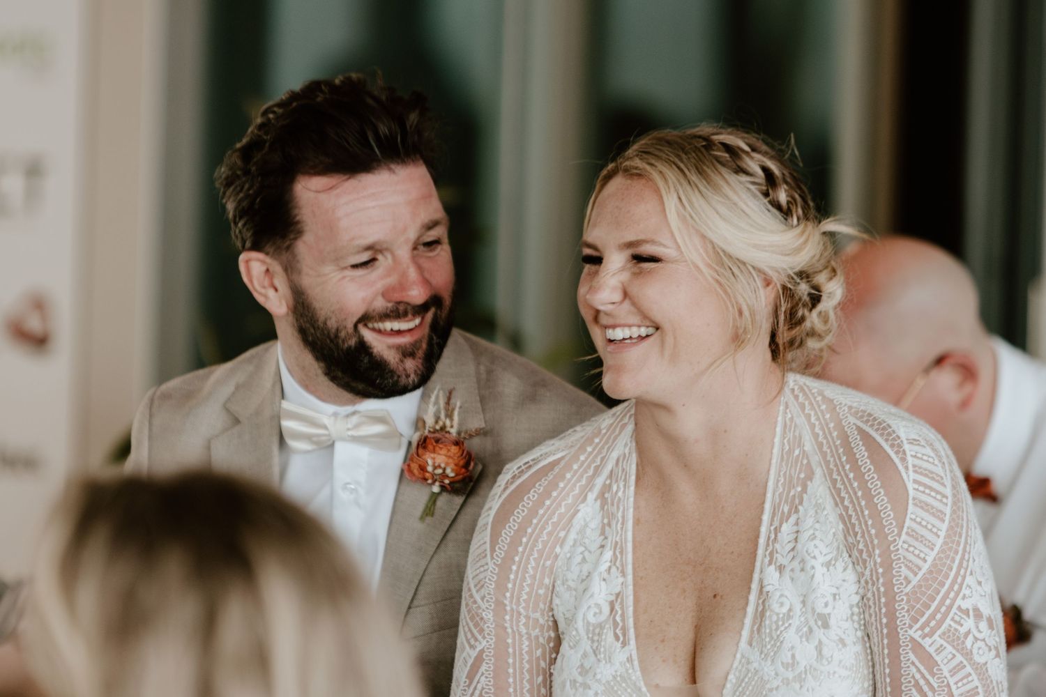 Happy couple laughs together during a wedding celebration in a rustic venue with natural lighting.