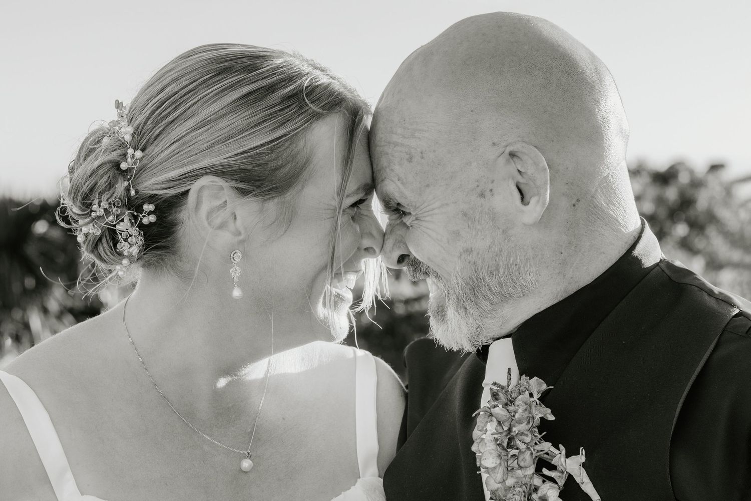 A tender black and white wedding moment captured between a couple touching foreheads, with the bride wearing a floral hairpiece.