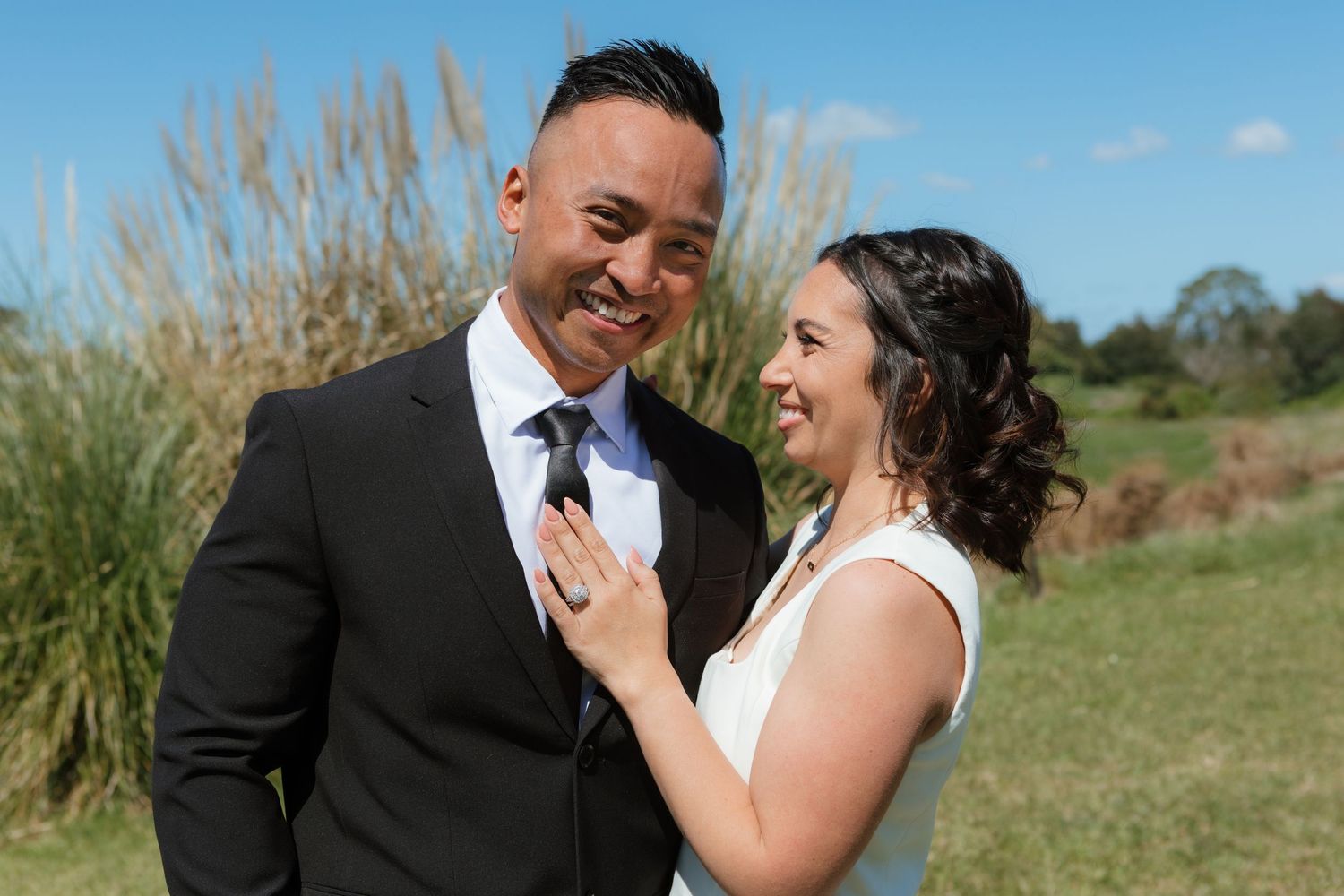 A happy couple shares a joyful moment together outdoors on their wedding day with tall ornamental grasses in background.