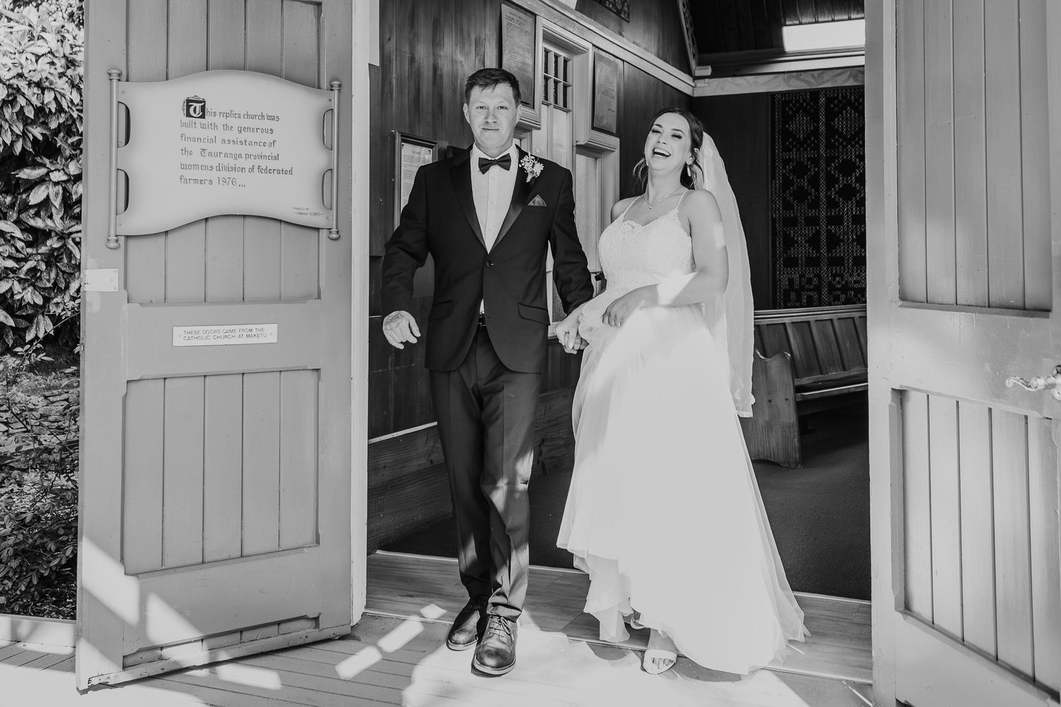 Joyful moment captured in black and white as newlyweds exit a church doorway together on their wedding day.