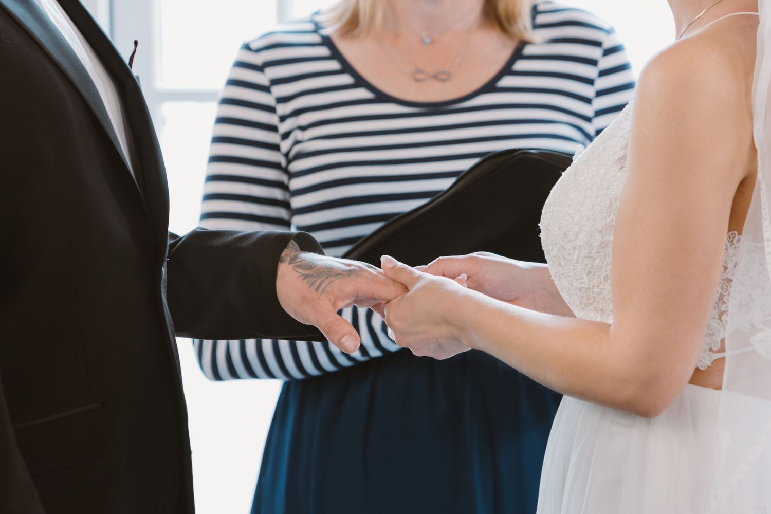 Small group gathered at indoor wedding ceremony near large arched windows.