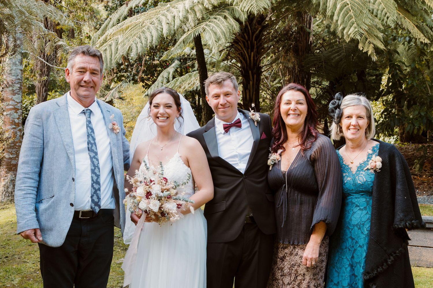 Wedding party gathers for formal photo under tropical ferns.