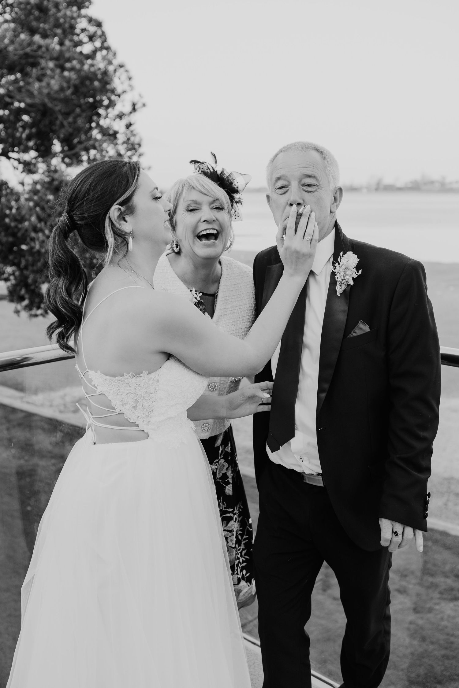 A joyful candid moment of laughter at an outdoor waterfront wedding celebration in black and white photography.