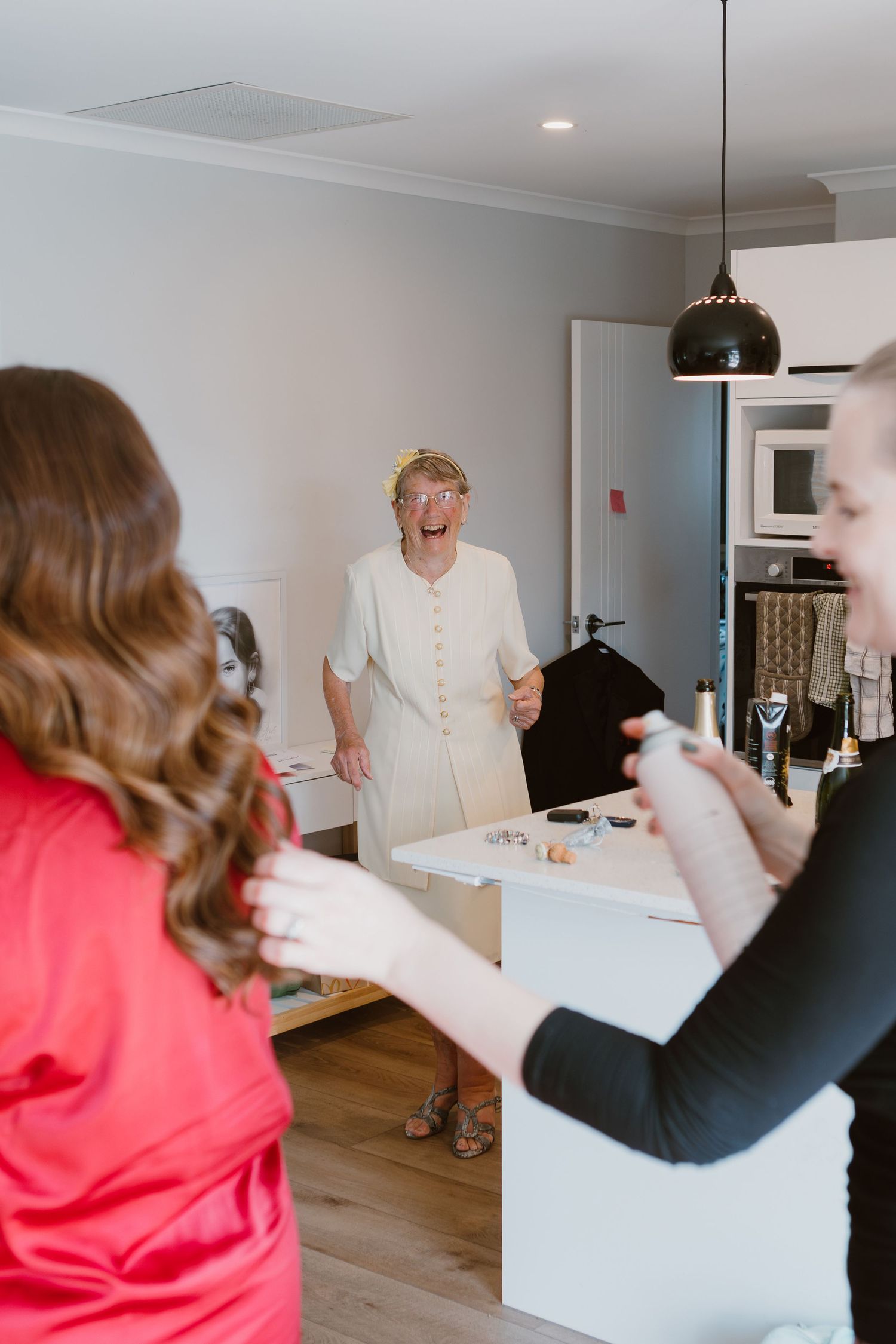 A group of people gather around a white box in a modern kitchen space with hardwood floors and white walls.