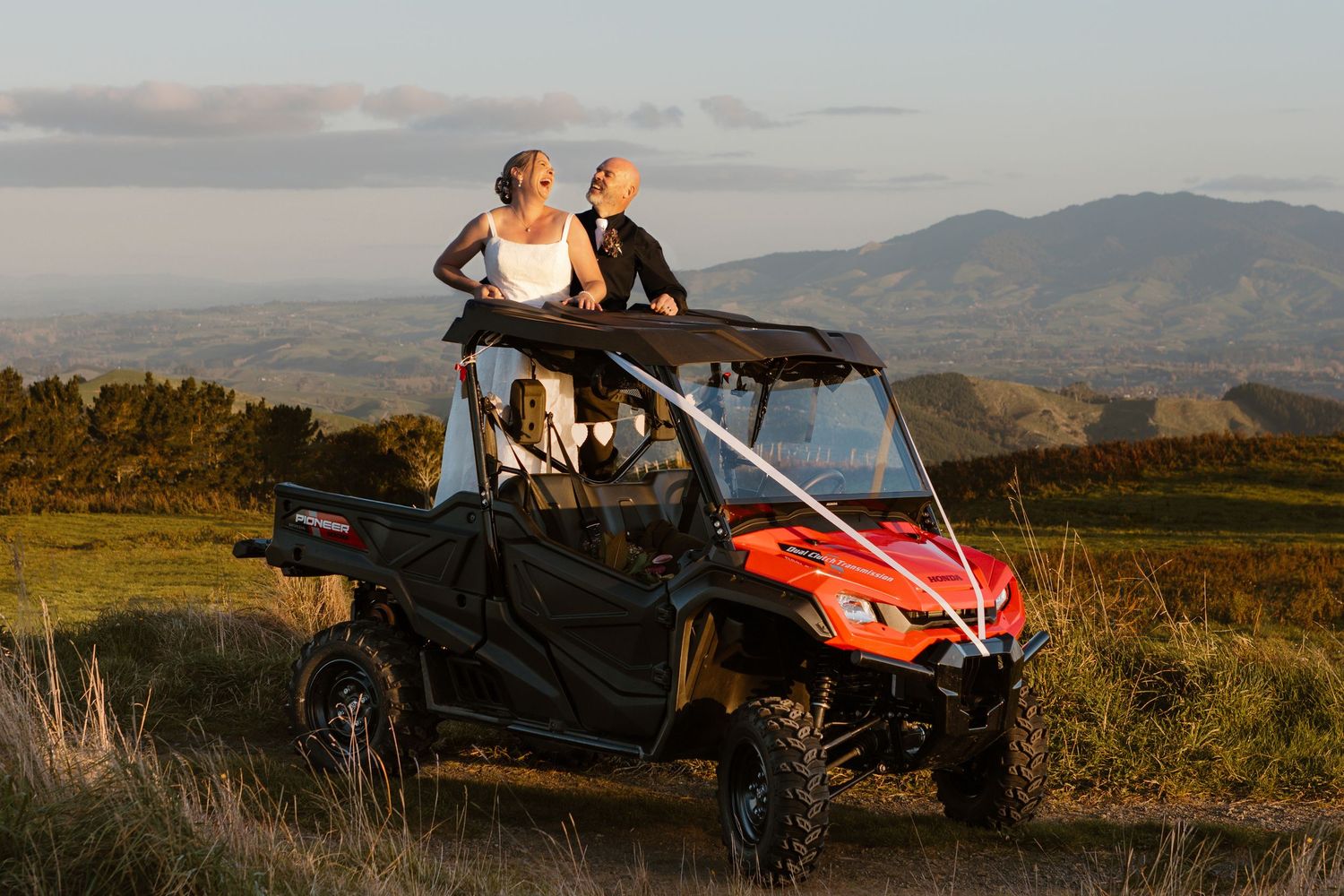 A couple enjoying sunset views from a red off-road UTV vehicle parked on a mountain overlook with scenic vistas.