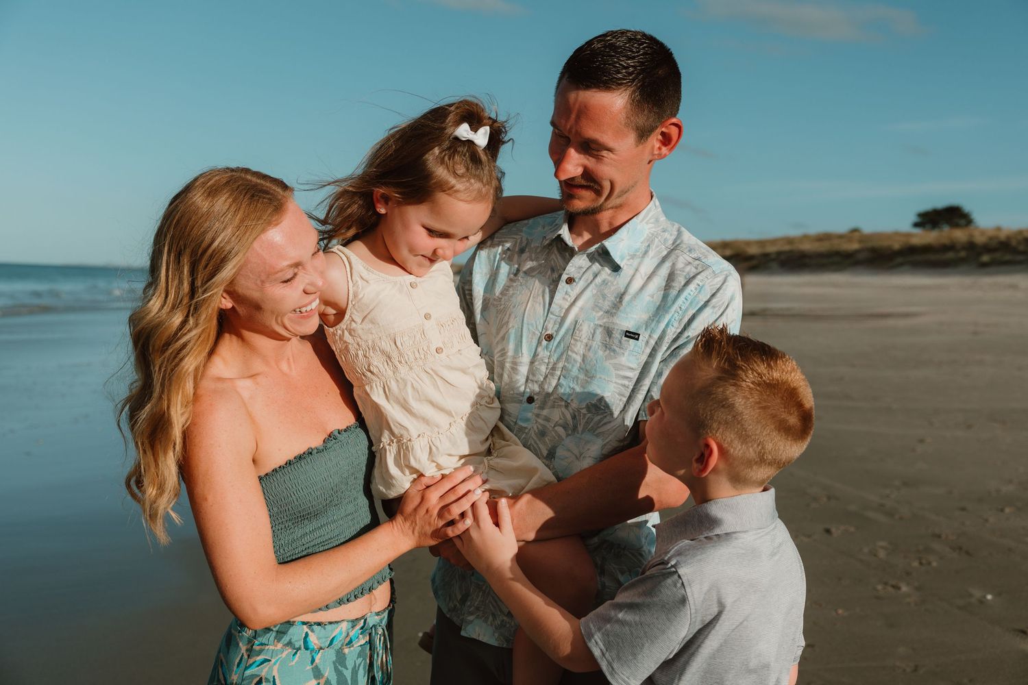 Family of four sharing a joyful moment together on a sunny beach, parents and two children looking down.