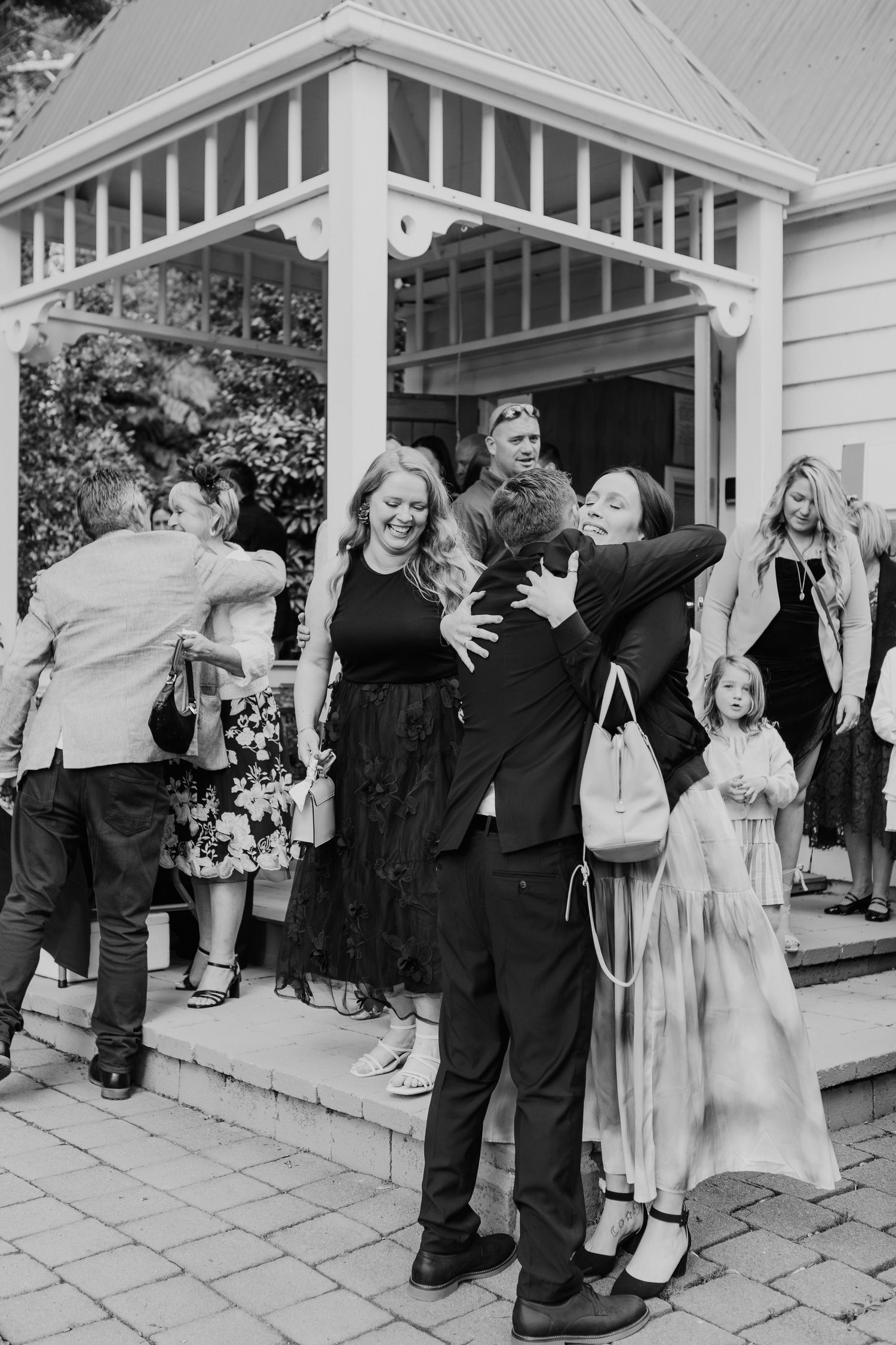 Black and white photo shows joyful celebration scene on a porch outside a house with decorative white trim.