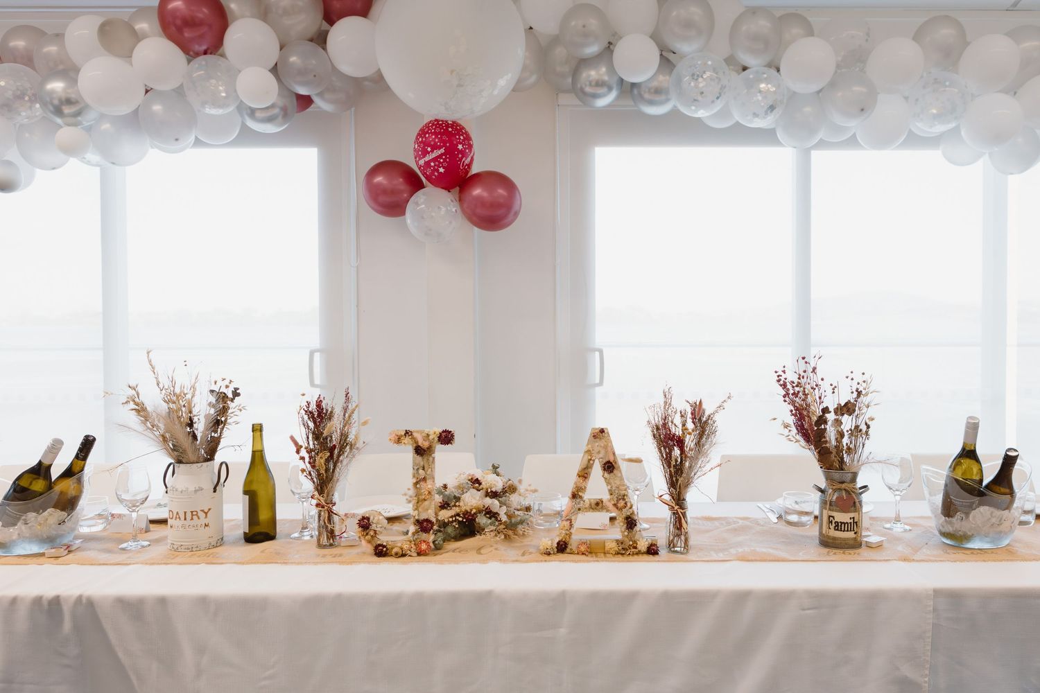 Pink and white paper lanterns decorate a dining table with rustic decor elements and window lighting for a celebration.