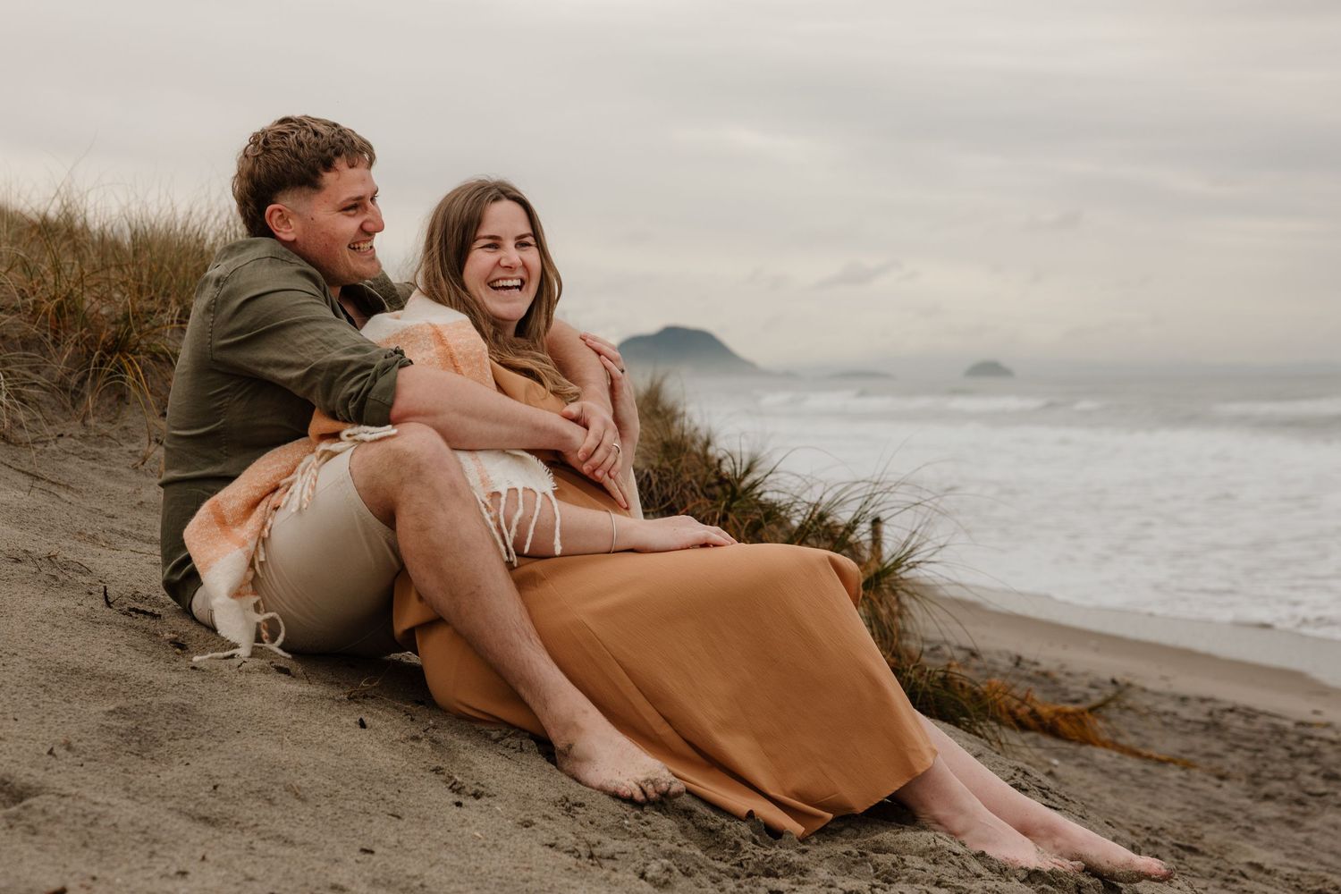 Couple sharing intimate moments together on a sandy beach during sunset along the coastline.