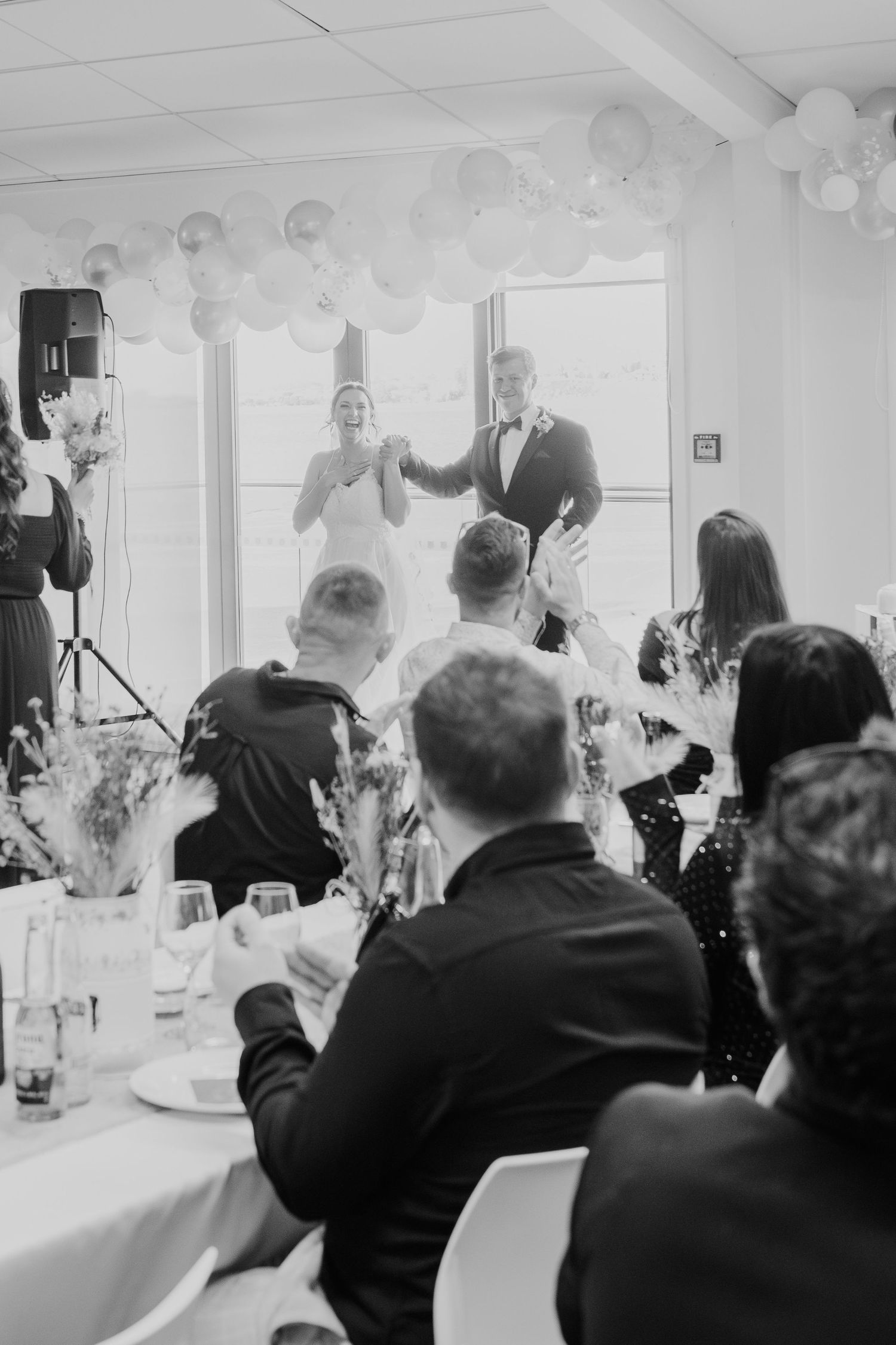 Wedding reception scene with guests watching a couple make their entrance under balloon decorations.
