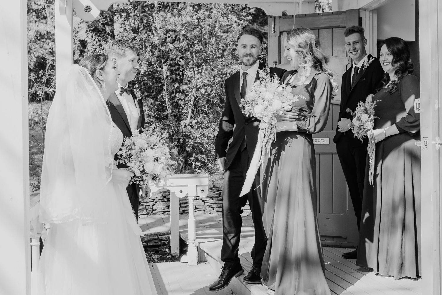 Wedding ceremony group enters covered outdoor walkway in formal attire.
