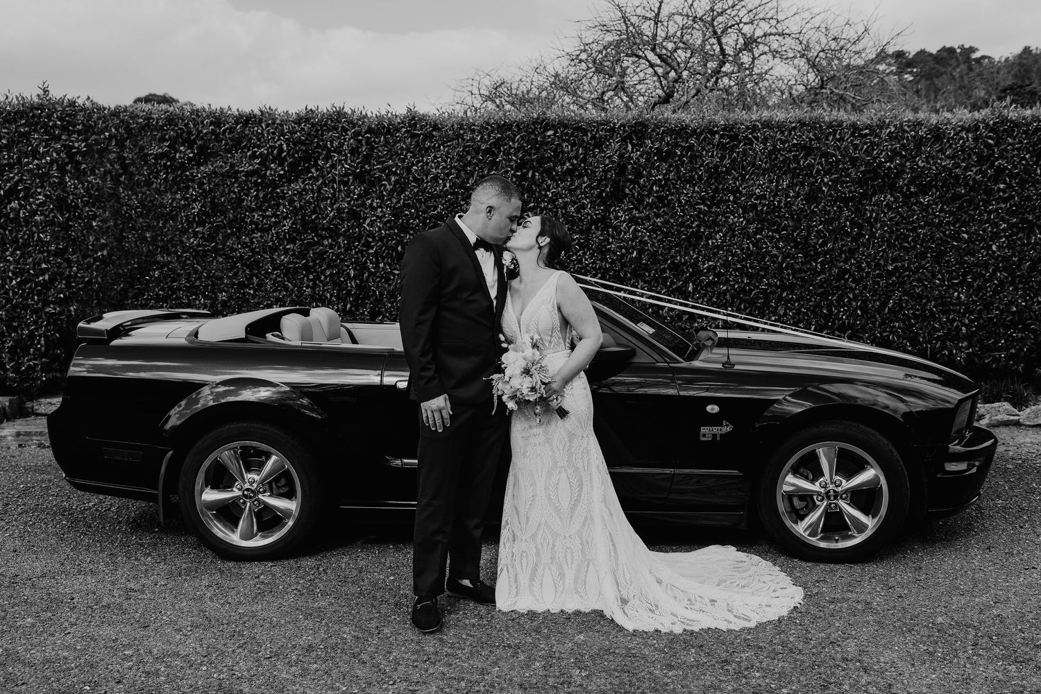 A series of black and white wedding photos showing a couple posing with a luxury car in an outdoor setting.