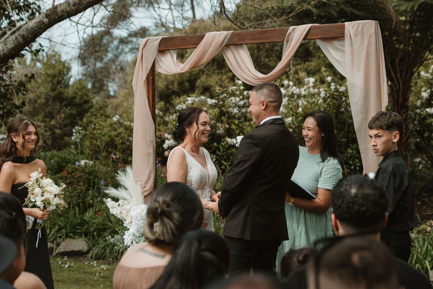 Outdoor wedding ceremony with draped white fabric decor and natural greenery in a garden setting.