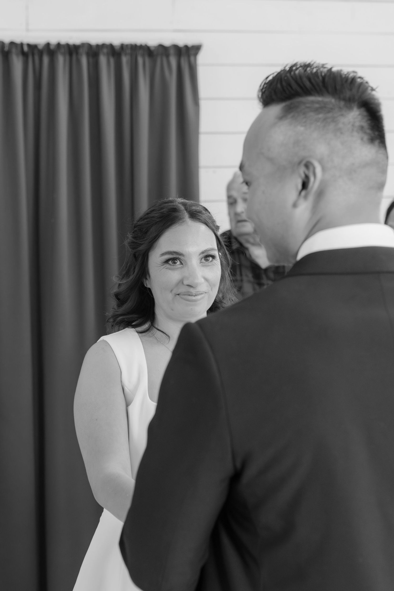 Black and white photograph of a bride and groom exchanging vows during an indoor wedding ceremony.