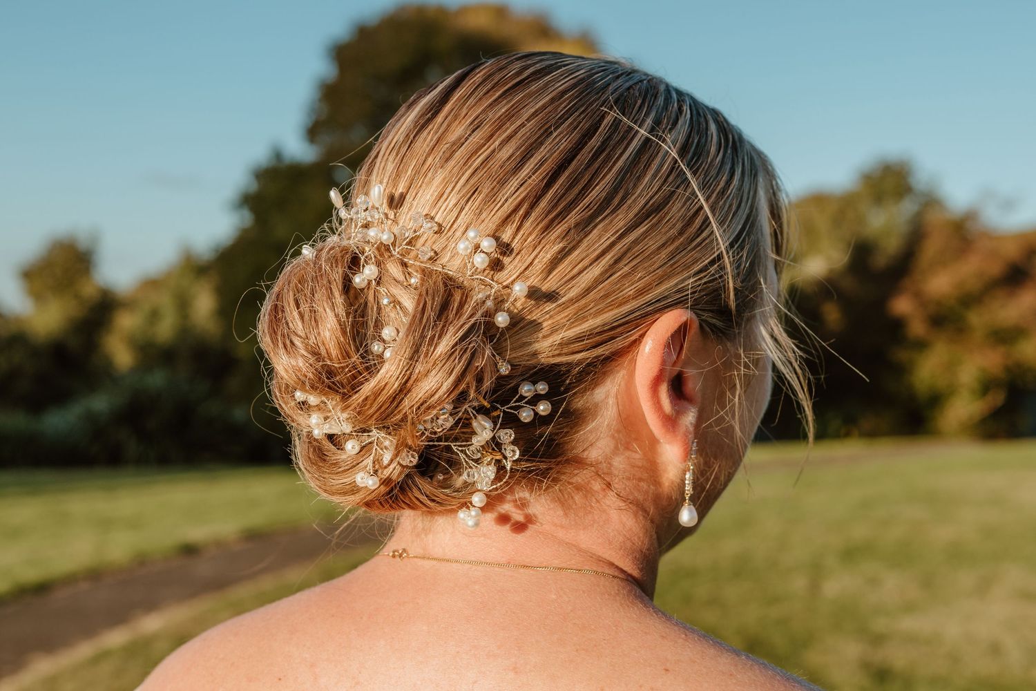Delicate floral hair accessories adorn an elegantly styled updo against a sun-lit outdoor background.