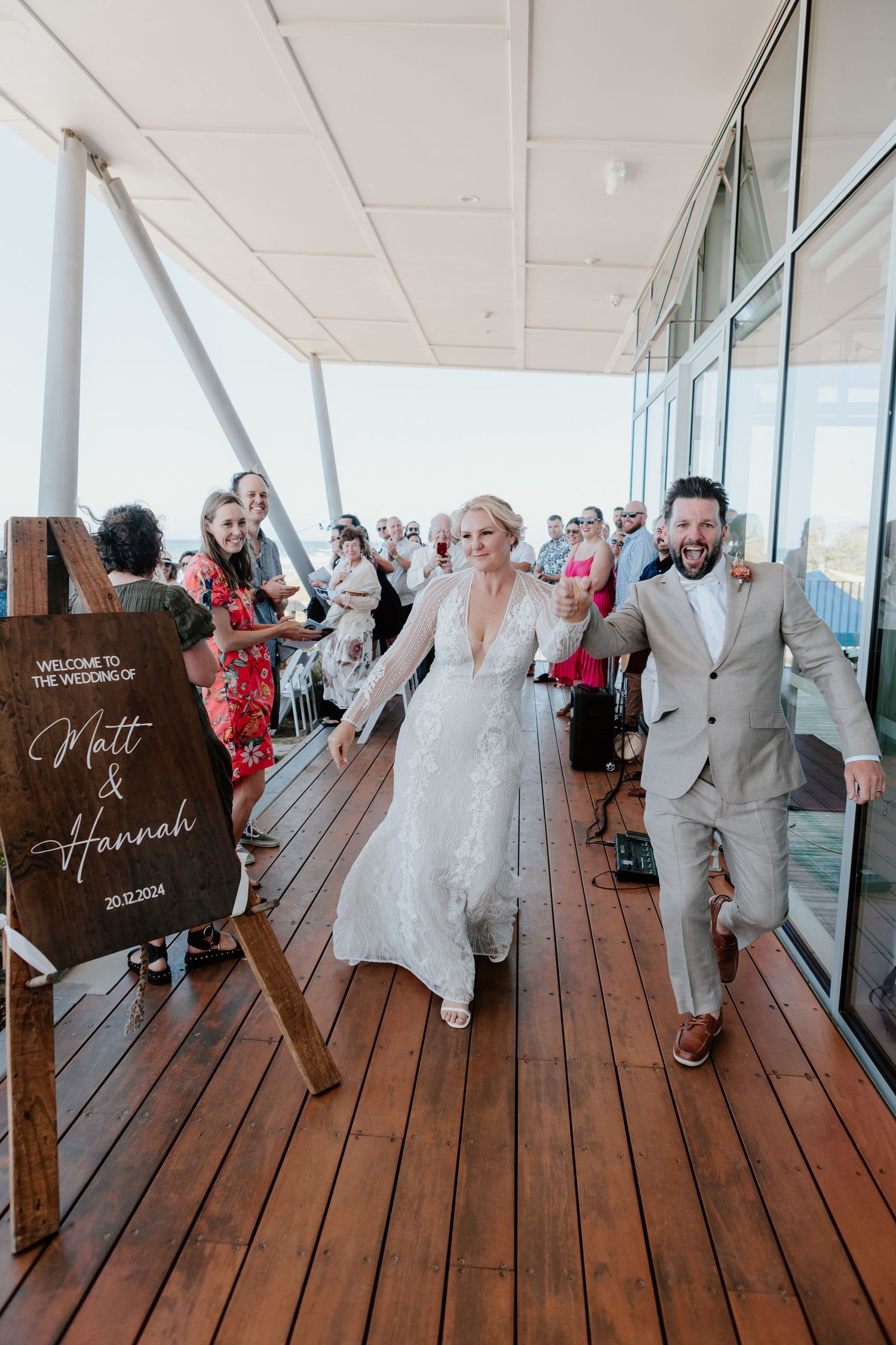 Panoramic view of wedding guests dancing and celebrating on a wooden deck overlooking the ocean.