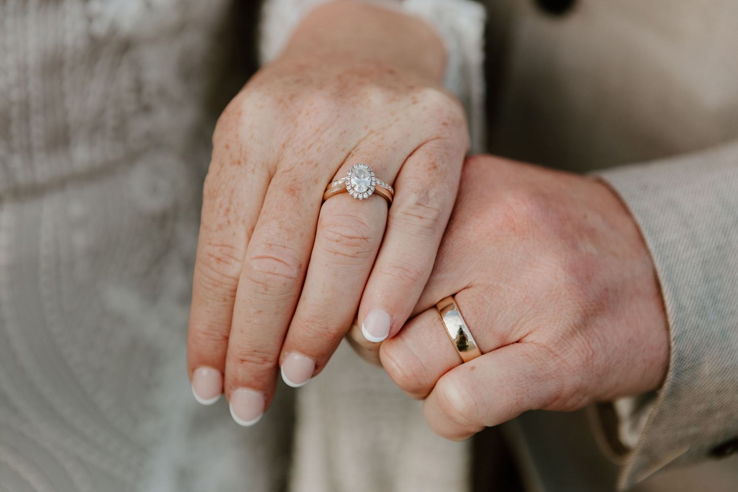 Two hands wearing wedding bands and an engagement ring with a diamond solitaire rest gently together.