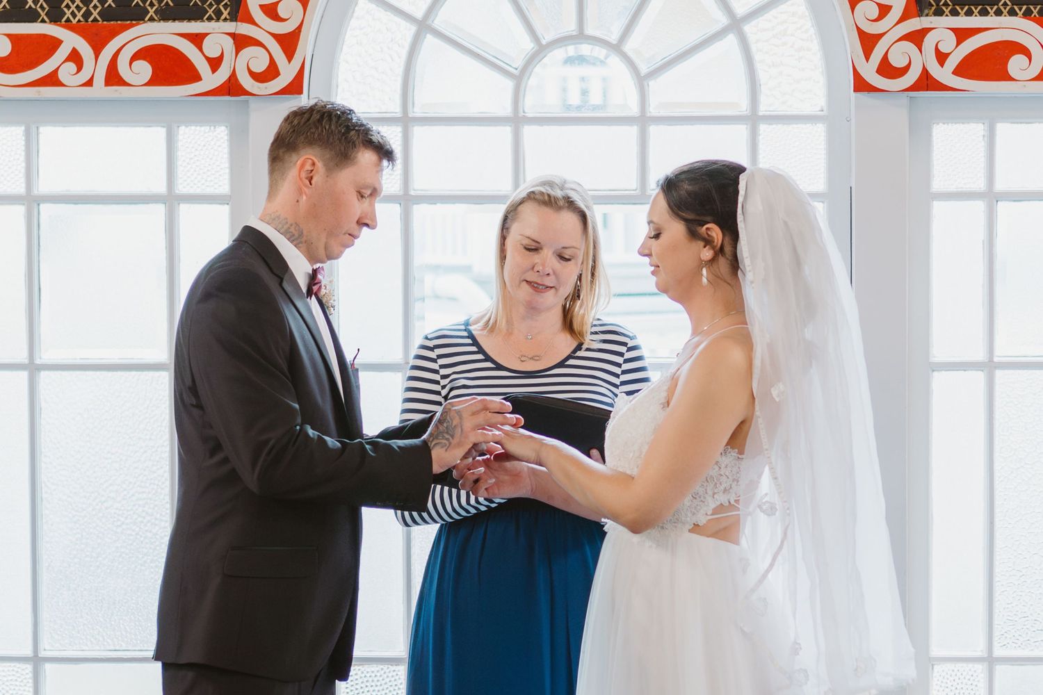 Joyful moments during a wedding document signing in front of large windows with red decorative accents.