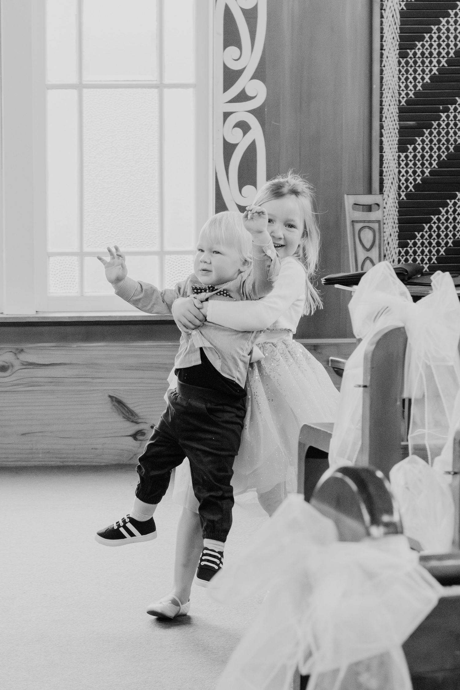 A black and white candid moment of children playing and dancing during what appears to be a formal event.