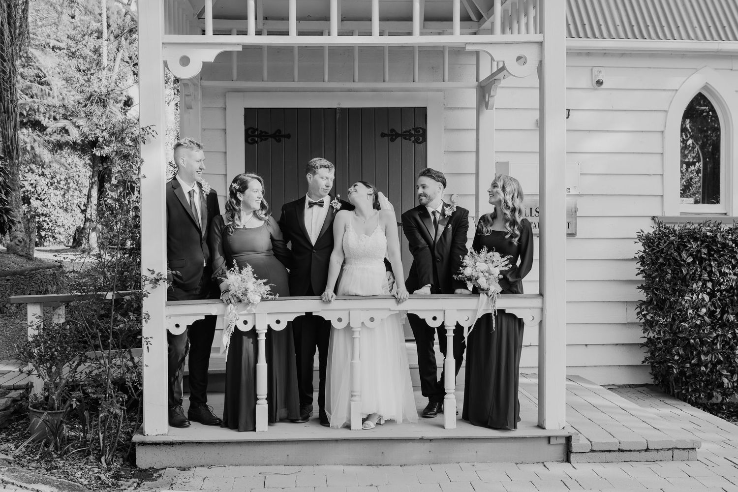 Black and white photo of a wedding party standing on a white porch at a vintage church entrance.