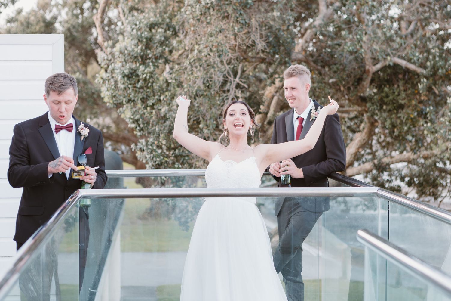 A wedding celebration on a glass balcony with raised arms and joyful expressions among the wedding party.