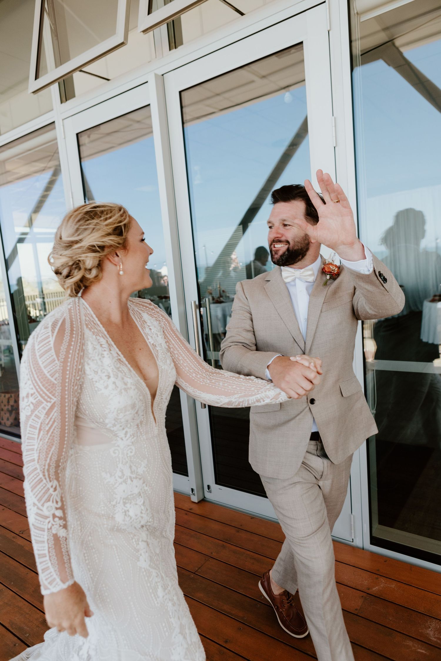 Couple shares a joyful moment on a modern deck with glass windows. Papamoa Surf Lifesaving Club Wedding