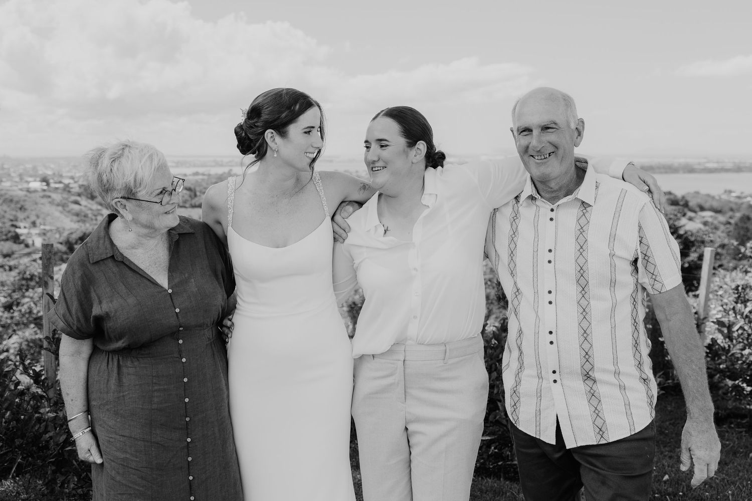 Black and white photo of a bride with family, smiling outdoors at a wedding celebration.