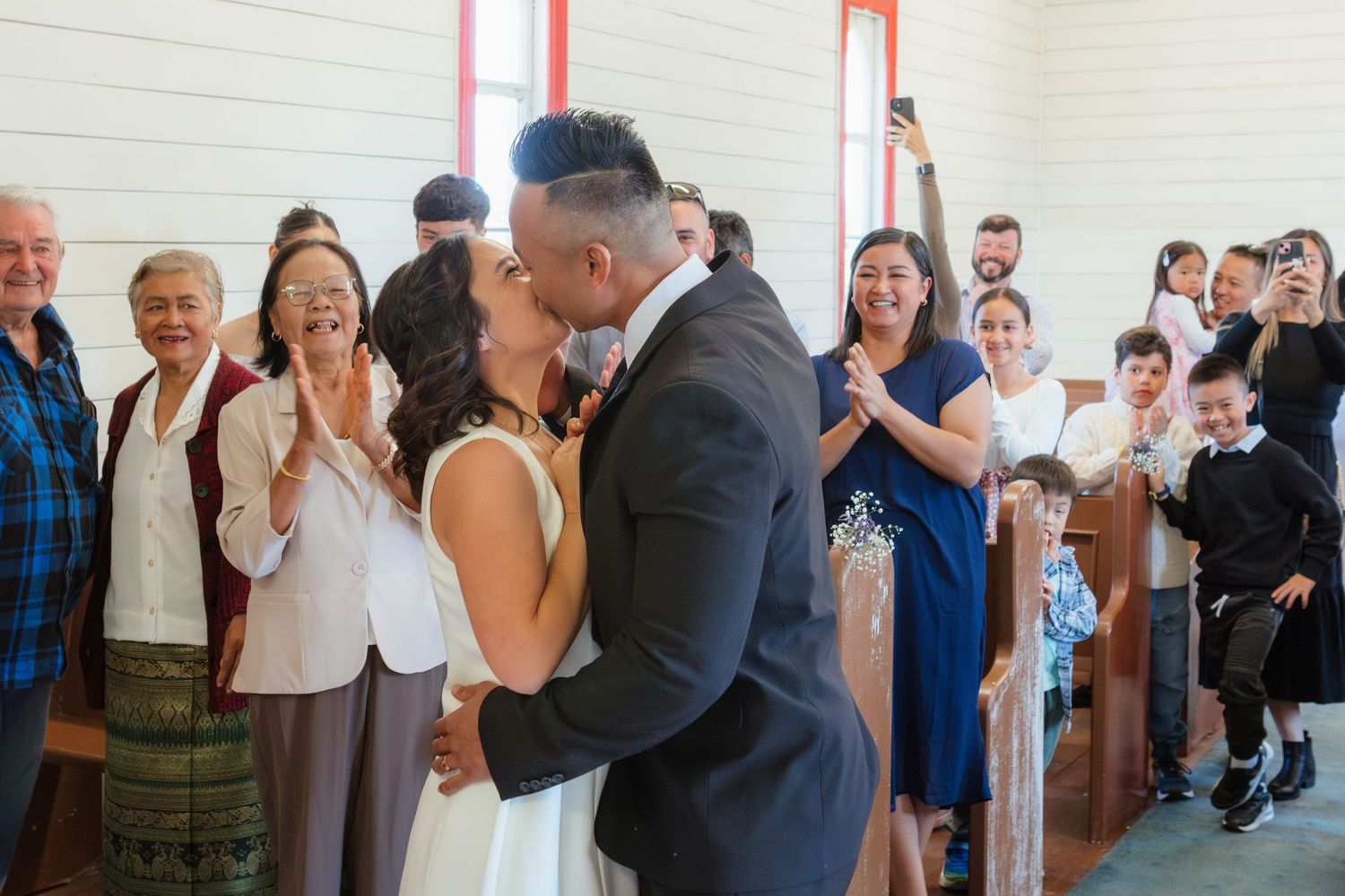 Wedding guests celebrate in a bright church interior with wooden benches.