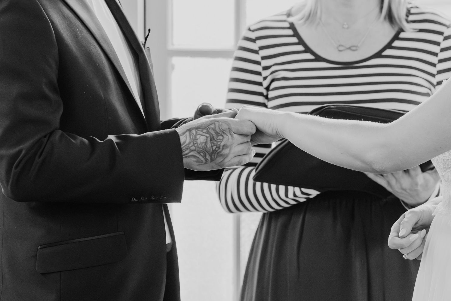Close-up black and white shot of hands during a wedding ceremony exchange.