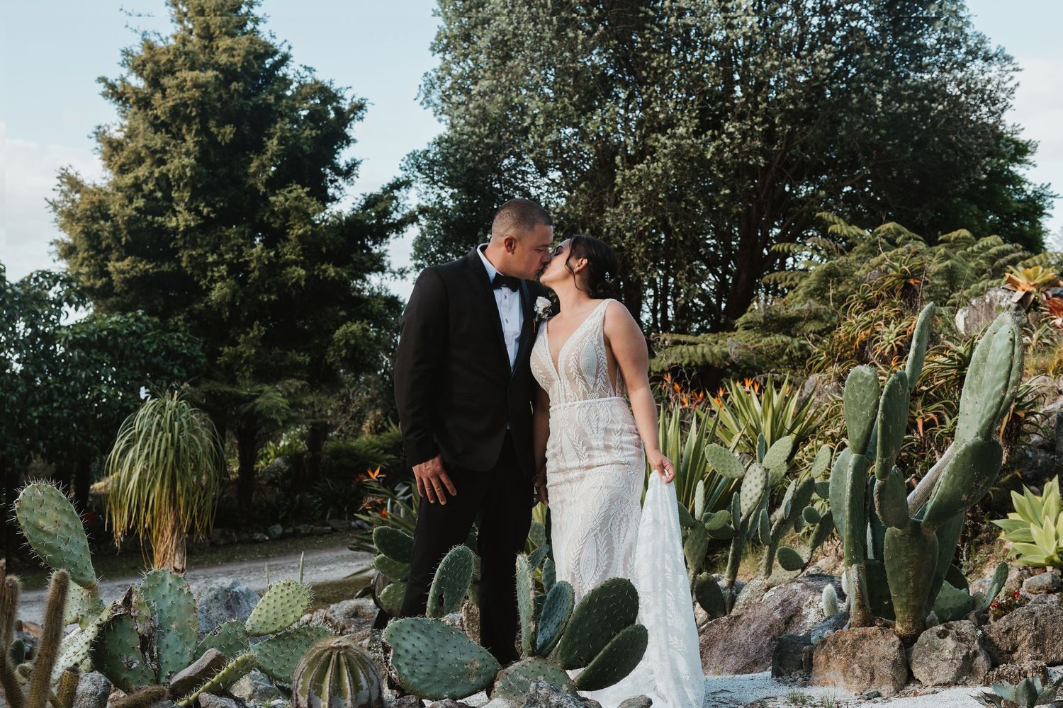 A couple shares an intimate moment in a garden filled with cacti and lush greenery during golden hour.