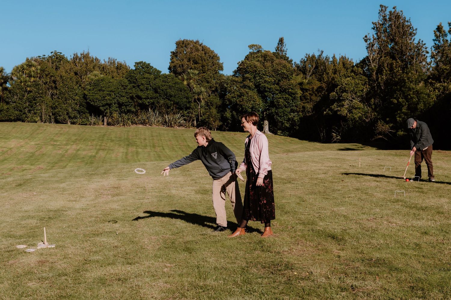 People playing croquet on a sunny grassy lawn with trees in the background during a relaxing afternoon.