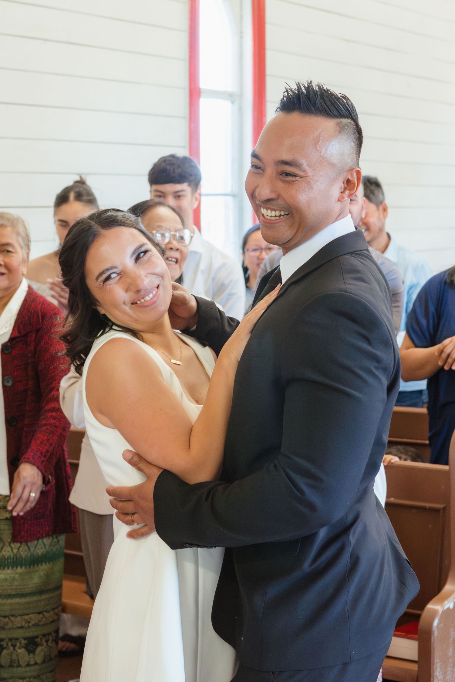 A joyful couple shares a dance in their wedding attire inside a church with guests visible in the background.