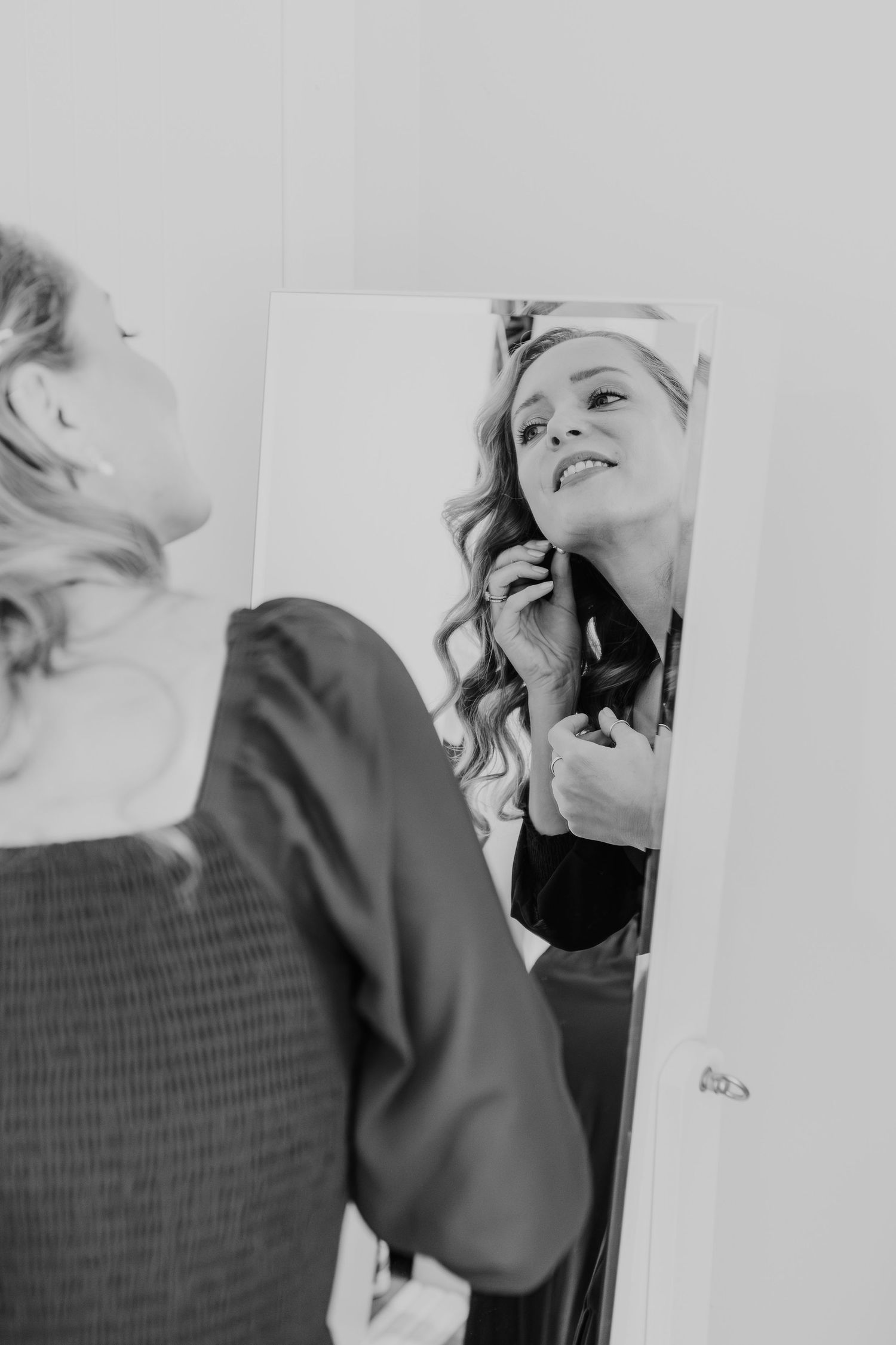 Black and white reflection in mirror shows someone with wavy hair smiling while getting ready.