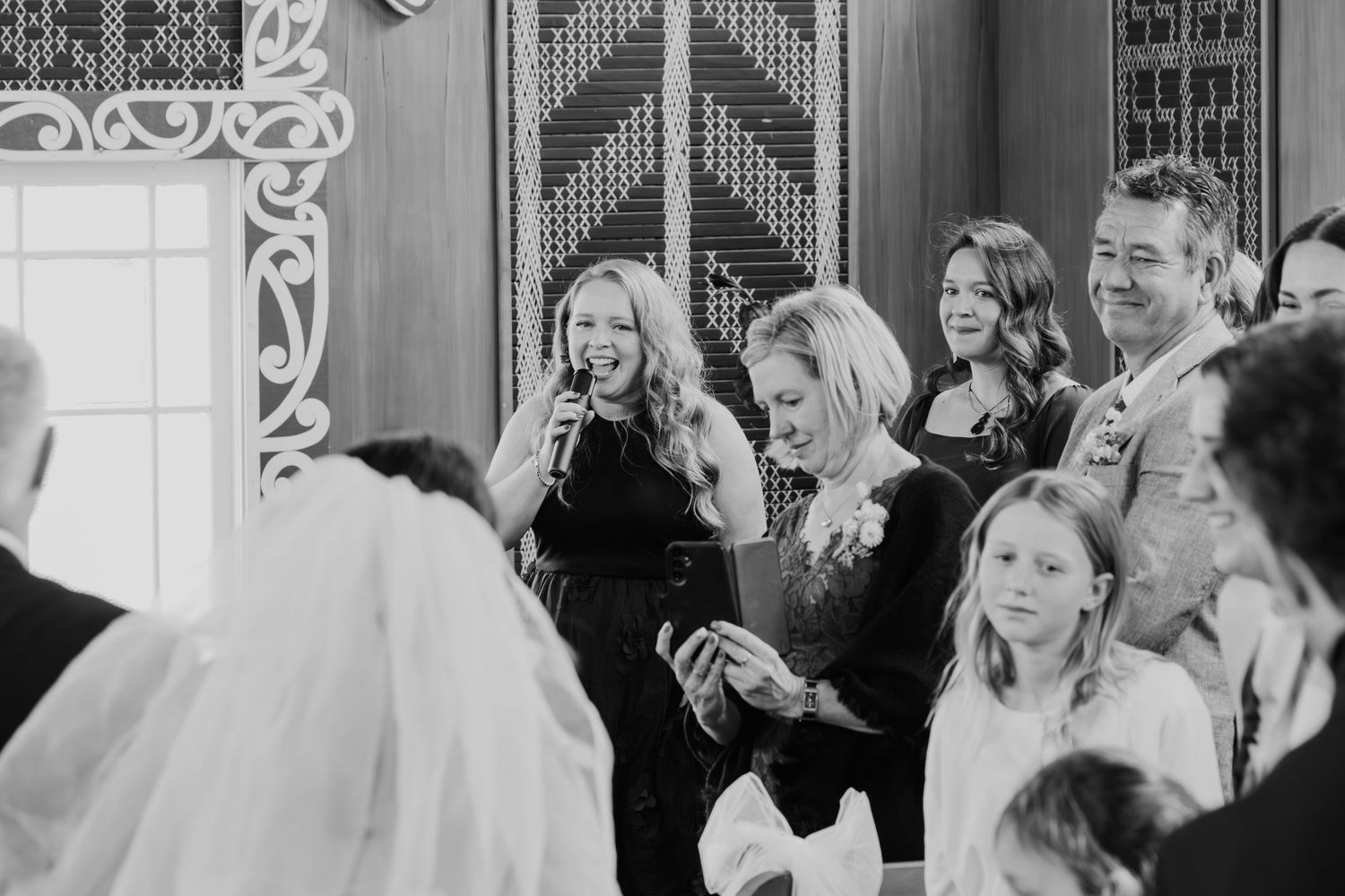 A joyful black and white wedding scene shows guests reacting with smiles and excitement during a celebration.
