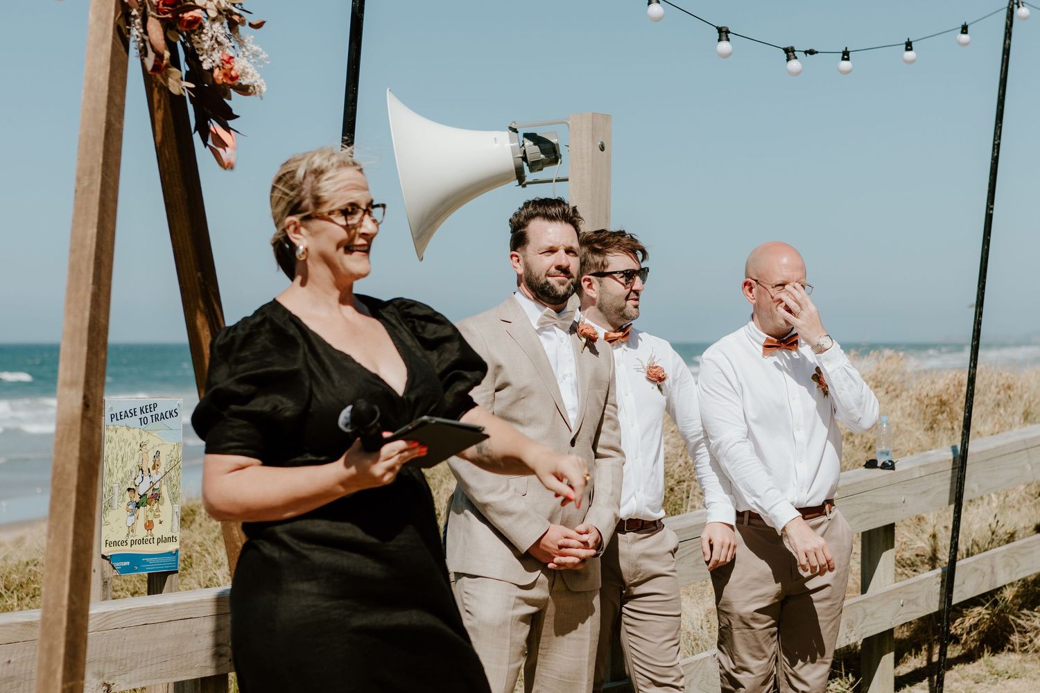 Outdoor beach wedding ceremony with string lights and ocean backdrop as guests gather on the sand.