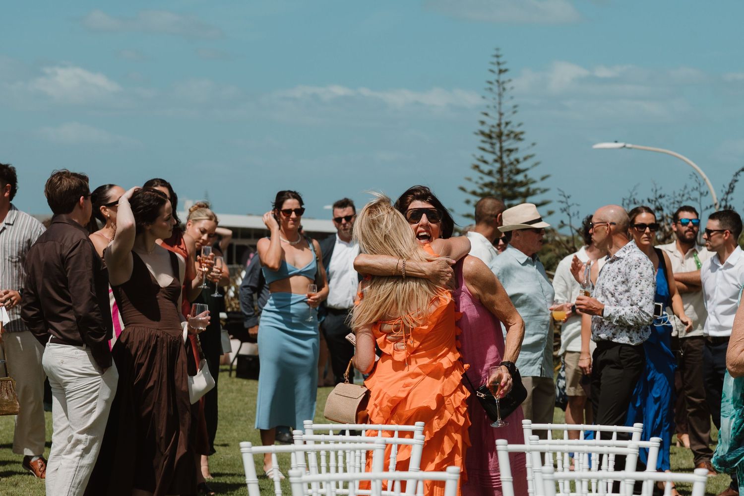 Guests embracing and celebrating at an outdoor wedding ceremony by the coast on a sunny day.