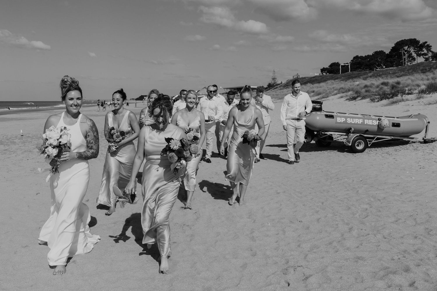 Bridal party walking joyfully on a sandy beach in black and white wedding photography.