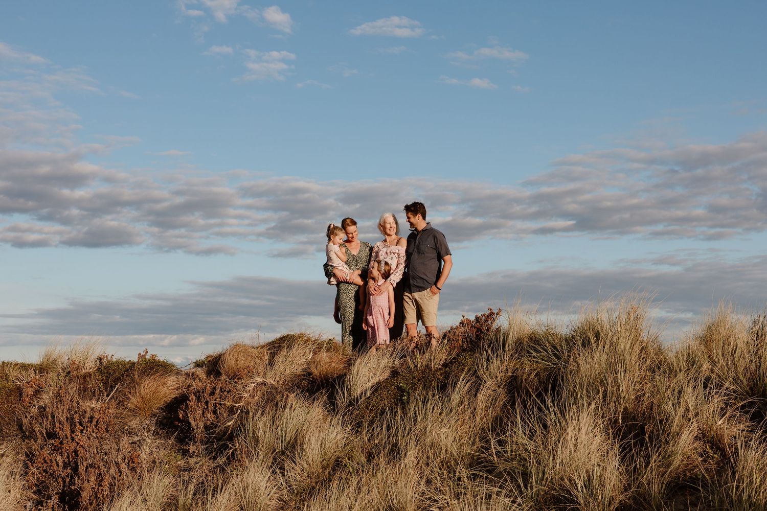 Family of four standing together on a grassy dune under a blue sky at golden hour.